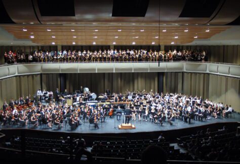 Full wind ensemble, choir, and orchestra performing on stage
